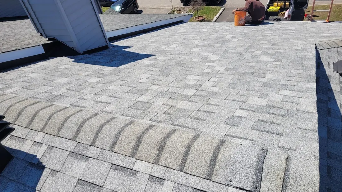 Grey shingle roof ridge cap with a worker in the distance